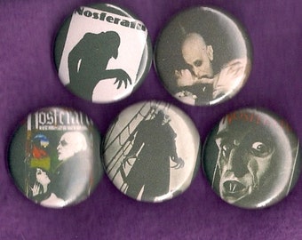May include: A collection of five round buttons with horror movie imagery. The buttons feature black and white images of vampires and movie titles like "Nosferatu" and "Lost City". The buttons are on a purple background.