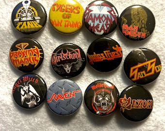May include: A collection of twelve round metal pinback buttons featuring various band logos and graphics. The buttons display text such as "Tygers of Pan Tang", "Iron Maiden", and "Judas Priest", with a variety of colors and designs.