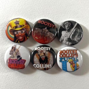 May include: A collection of six round pinback buttons featuring images of Bootsy Collins. The buttons display colorful portraits and black and white images of the musician, with text that reads "BOOTSY" and "BOOTSY COLLINS FUNK".