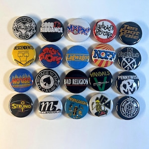May include: A collection of twenty-one round pinback buttons with various band logos and text. The buttons feature a variety of colors, including black, white, blue, yellow, and red. The buttons are arranged in a grid pattern.