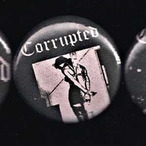 May include: Three black and white button badges with the word "Corrupted" printed in white. The badges feature different images, including a woman in a dress and a figure with a guitar.