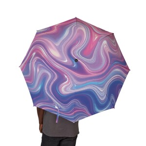Pode incluir: Um guarda-chuva aberto com um padrão marmoreado em espiral em tons de rosa, roxo e azul. A cobertura exibe um design fluido, semelhante a um líquido, com gradientes claros e escuros que se misturam pela superfície, centrado por um eixo preto.