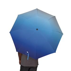 May include: A blue gradient umbrella with a black top and a light blue handle. The umbrella is open, displaying a range of blue hues from light to dark. The umbrella has a white tag with text.