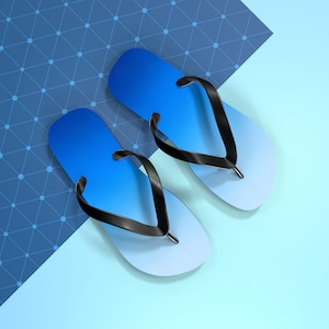 May include: A pair of blue and white gradient flip-flops with black straps. The sandals are arranged on a light blue surface with a geometric pattern in the background. The flip-flops are a summer footwear item.