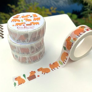 Op de afbeelding: Drie rollen washi tape met een capybara-ontwerp. De tape is wit met een lichtbruin capybara-ontwerp. De tape ligt op een wit oppervlak. De tekst op de tape luidt "Eloise Narrigan eloisenarrigan.com".