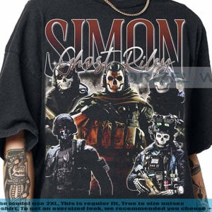 May include: Black t-shirt featuring a graphic of a skull-faced character with the name "SIMON Ghost Riley" in a distressed font. The design includes multiple figures in tactical gear. The text at the bottom provides sizing information.