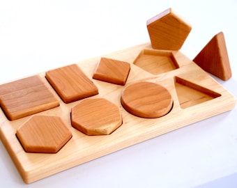 May include: Wooden shape sorting toy with a variety of geometric shapes, including a circle, square, triangle, hexagon, and pentagon. The shapes are made of natural wood and have a smooth finish.