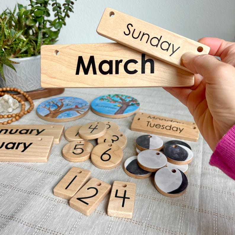 May include: A set of wooden calendar pieces including rectangular tiles with the text Sunday, March, January, Monday, and Tuesday, circular number tiles, rectangular number tiles, circular moon phase tiles, and two circular seasonal illustrations.