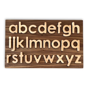 May include: Wooden alphabet puzzle with the letters a-z in a light wood color on a dark wood background.