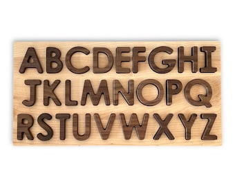 May include: Wooden alphabet puzzle with the letters A through Z cut out in a light brown wood. The letters are made of a darker brown wood and are raised from the board.