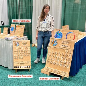May include: A wooden perpetual calendar set featuring a light wood finish, circular date markers, and interchangeable month and year tiles. The boards include sections for weather, moon phases, and days of the week, labelled Home Calendar, Classroom Calendar, and School Calendar.