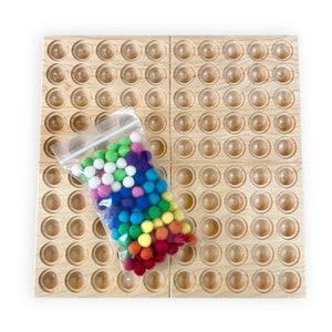 Könnte beinhalten: Ein Holzbrett mit 100 runden Vertiefungen, zum Sortieren und Zählen von bunten Filzkugeln. Die Kugeln werden in einem durchsichtigen Plastikbeutel aufbewahrt.