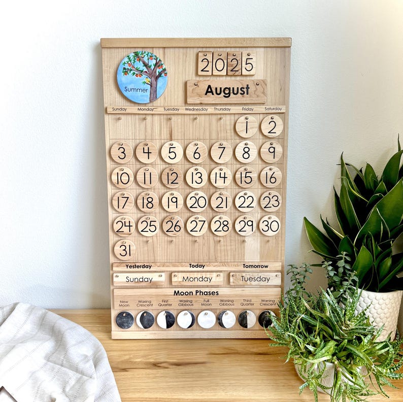 May include: A wooden perpetual calendar board featuring the year 2025 and the month of August. It includes a circular summer tree illustration, numbered wooden discs for dates 1 through 31, day-of-the-week labels, and a moon phase tracker.
