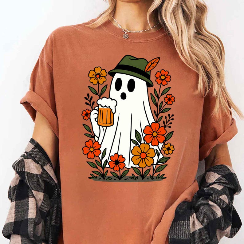 May include: Rust-colored t-shirt featuring a cartoon ghost wearing a green hat with a feather, holding a beer stein. The ghost is surrounded by orange and yellow flowers and green foliage. The shirt has short sleeves and a relaxed fit.