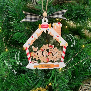 May include: A festive gingerbread house Christmas ornament, featuring a clear centre filled with gingerbread figures and the text "THE HORN FAMILY". The ornament has a red and white striped border, a chimney, and a black and white plaid bow. The year "2025" is displayed on the roof.