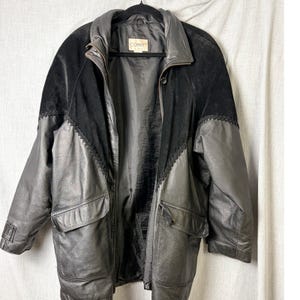 May include: A vintage black leather jacket with a suede upper panel and decorative stitching. The jacket features a notched collar, two front pockets, and a button closure. The label reads "CONNIT".