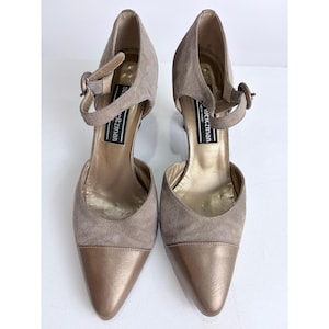 May include: A pair of taupe suede and metallic bronze pointed-toe pumps with ankle straps. The heels are approximately 3 inches high. The brand name "Stuart Weitzman" is visible on the inner sole.