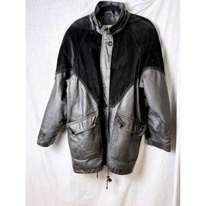May include: A black jacket featuring a combination of smooth leather and suede textures. The garment includes a high collar, a front zipper closure, two large flap pockets at the waist, and a decorative zigzag stitched seam across the chest.