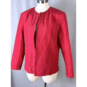 May include: A red jacket with a textured, diagonal pattern. The jacket has long sleeves and a collarless design. The garment is displayed on a mannequin. The jacket is a solid, vibrant red color.