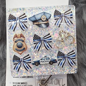 May include: A police-themed badge reel with a clear, glittery background. The design includes police badges, a police hat, handcuffs, and a police car. The text on the reel says "POLICE".