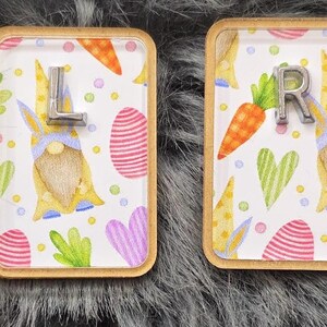 May include: Two rectangular wooden-framed decorative magnets. One magnet has the letter "L" and the other has the letter "R". Both magnets feature a colorful Easter-themed design with gnomes, carrots, eggs, and hearts.