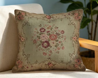 May include: A square throw cushion featuring a light sage green fabric base with a central floral bouquet in shades of pink, burgundy, and cream. The design includes a decorative border with small rose motifs and scrolling vine patterns.