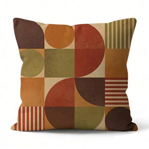 Könnte beinhalten: Quadratisches Kissen mit geometrischem Design. Das Kissen zeigt ein Muster aus Kreisen, Quadraten und Streifen in Braun-, Orange- und Grüntönen. Das Design hat eine Vintage- und Retro-Ästhetik.