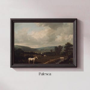 May include: Framed landscape painting featuring white horses grazing in a field near a body of water. The artwork has a dark wooden frame and depicts a pastoral scene under a cloudy sky. The word "Palesca" is printed at the bottom.