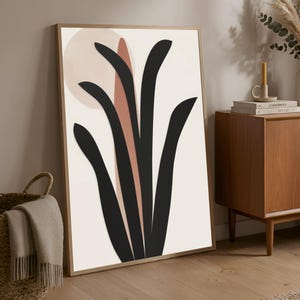 May include: Framed abstract art print featuring a minimalist design. The artwork showcases black, curved shapes against a cream background, with a peach-colored circle and a vertical stripe. The print is encased in a light brown wooden frame, suitable for home decor.