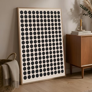 Pode incluir: Uma impressão artística emoldurada com um padrão de círculos pretos espaçados em um fundo creme. A obra de arte é apresentada em uma moldura de madeira marrom clara. A impressão está encostada em uma parede, adequada para decoração de casa moderna.