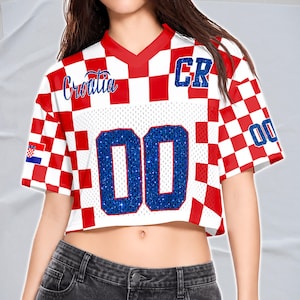 May include: Cropped white and red checkered jersey with the word "Croatia" in blue script. The jersey has the number "00" in blue glitter and the letters "CR" on the shoulder.