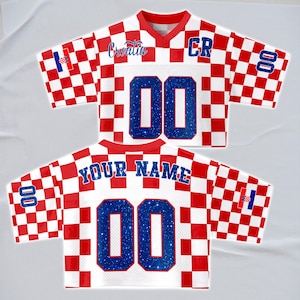 May include: A white and red checkered jersey with the word "Croatia" in blue script. The jersey has the number "00" in blue glitter on the front and back. The sleeves have the Croatian flag and the number "00". The back of the jersey says "YOUR NAME".