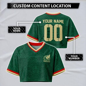 Op de afbeelding: Een groen kort shirt met een V-hals met rode en gouden randen. De voorkant toont een cirkelvormige afbeelding in Azteekse stijl en een Mexico-logo. De achterkant toont de tekst YOUR NAME en het nummer 00 in goud met een gebarsten textuureffect.