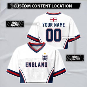 Könnte beinhalten: Ein weißes Kurzarmtrikot mit roten und blauen Akzenten, das vorne den Schriftzug ENGLAND und ein Wappen zeigt. Auf der Rückseite befinden sich der Text YOUR NAME, die Nummer 00 und eine englische Flagge. Textfelder markieren die anpassbaren Bereiche.