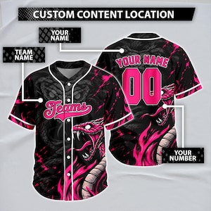 Könnte beinhalten: Ein schwarz-pinkes Baseballtrikot mit einer Grafik einer Schlange mit offenem Maul und Fangzähnen. Auf der Vorderseite steht das Wort Teams in pinker Schreibschrift, während auf der Rückseite der Text Your Name und die Nummer 00 in Pink zu sehen sind.