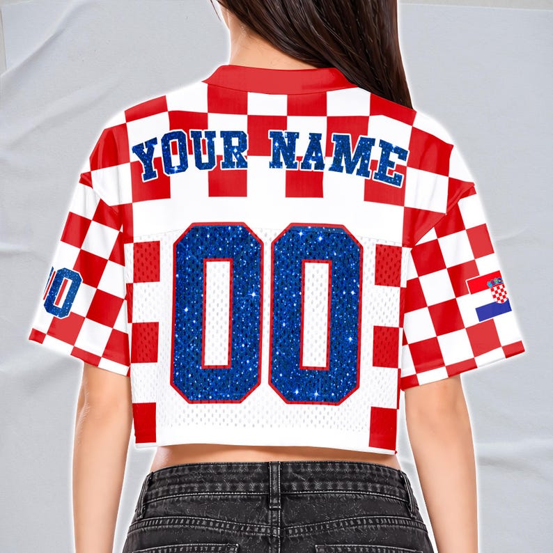 May include: Cropped white and red checkered jersey with the text "YOUR NAME" in blue. The jersey has the number "00" in blue glitter and a Croatian flag on the sleeve. The jersey has a red collar and sleeve trim.