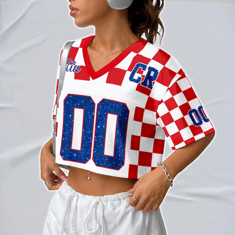 May include: A cropped white and red checkered jersey-style top with blue glitter numbers and lettering. The top has a V-neck and short sleeves. The number "00" is prominently displayed on the front.