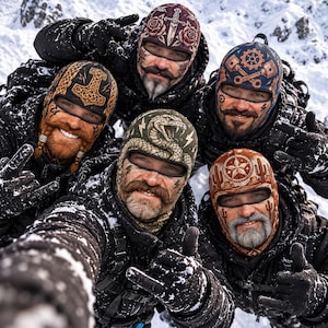 May include: Five balaclavas featuring distinct graphic prints including a dagger with roses, a hammer, mechanical gears, a coiled snake with lightning bolts, and a desert landscape with cacti and a star, worn by individuals in snowy conditions.