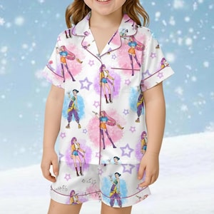 May include: White pajama set with a repeating cartoon character print. The short-sleeved top and shorts feature a button-down design and are trimmed with a dark purple piping. The print includes stars and figures in various poses.