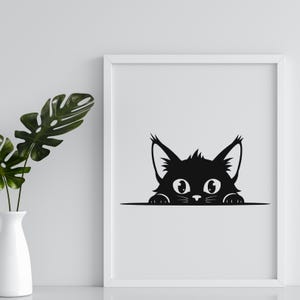 May include: A framed black and white print featuring a stylized cat peeking over a horizontal line. The cat has large, round eyes, pointed ears, and a fluffy appearance. The print is displayed on a white background.