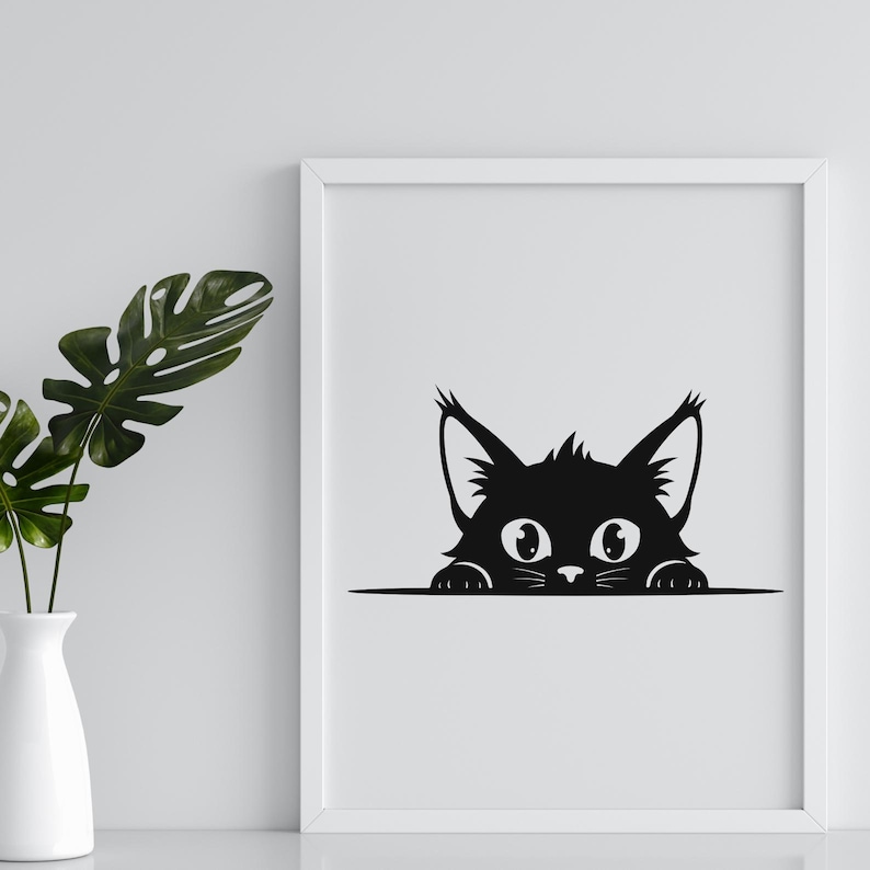 May include: A framed black and white print featuring a stylized cat peeking over a horizontal line. The cat has large, round eyes, pointed ears, and a fluffy appearance. The print is displayed on a white background.