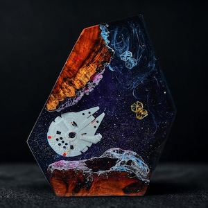 Könnte beinhalten: Ein Kunstwerk aus Harz mit einer Weltraumszene mit einem Millennium Falken, Tie-Jägern und einem Galaxie-Design. Das Kunstwerk hat einen Holzsockel mit Orange- und Brauntönen, und die Weltraumszene ist vor einem dunkelvioletten Hintergrund dargestellt.