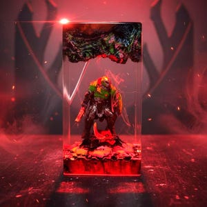 May include: A detailed resin sculpture of a character from the video game Doom, encased in a clear rectangular block. The figure is clad in green and bronze armor, holding a weapon and shield. The base and top of the block feature textured, colorful elements, with a red glow.