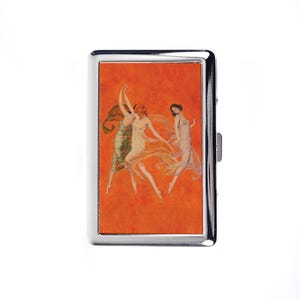 May include: A silver cigarette case featuring an art deco image of three dancing women in flowing gowns against an orange background. The case has a rectangular shape with a hinged closure.