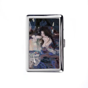 May include: A silver cigarette case with a painting of a woman with long dark hair. The artwork uses blues, purples, and flesh tones. The woman is reclining, with her arms crossed. The case has a shiny, reflective surface.