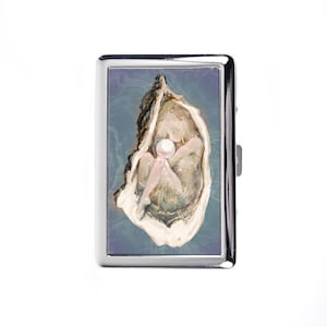 May include: A silver cigarette case featuring an artistic depiction of a pearl within an oyster shell. The artwork uses muted tones of beige, pink, and blue, creating a serene and elegant aesthetic. The case has a polished, reflective surface.