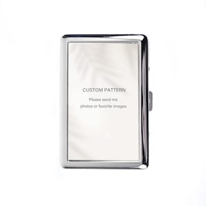 May include: A rectangular, silver-colored metal case with a hinged lid. The front of the case features a white rectangle with the text "CUSTOM PATTERN" and a request to send photos or favorite images. The case has a shiny, reflective surface.