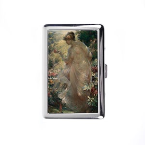 May include: A silver cigarette case featuring a classical painting of a woman in a flowing gown, holding a small object. The artwork is set in a garden with flowers and greenery. The case has a shiny, metallic finish.