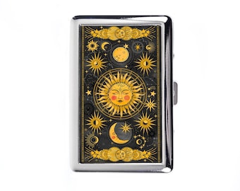 May include: A silver metal cigarette case with a celestial design. The case features a black background with gold illustrations of the sun, moon, stars, and other celestial bodies. The sun has a face with rosy cheeks.