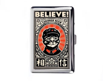 Puede incluir: Un estuche de cigarrillos de metal plateado con un diseño gráfico de un gato con sombrero y estrella roja. El texto "BELIEVE! CHAIRMAN MEOW" está sobre el gato, con caracteres chinos y "LONG LIVE THE KITTY" debajo.
